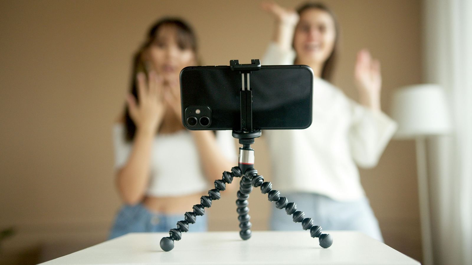 Two women recording a video on a smartphone tripod in a room