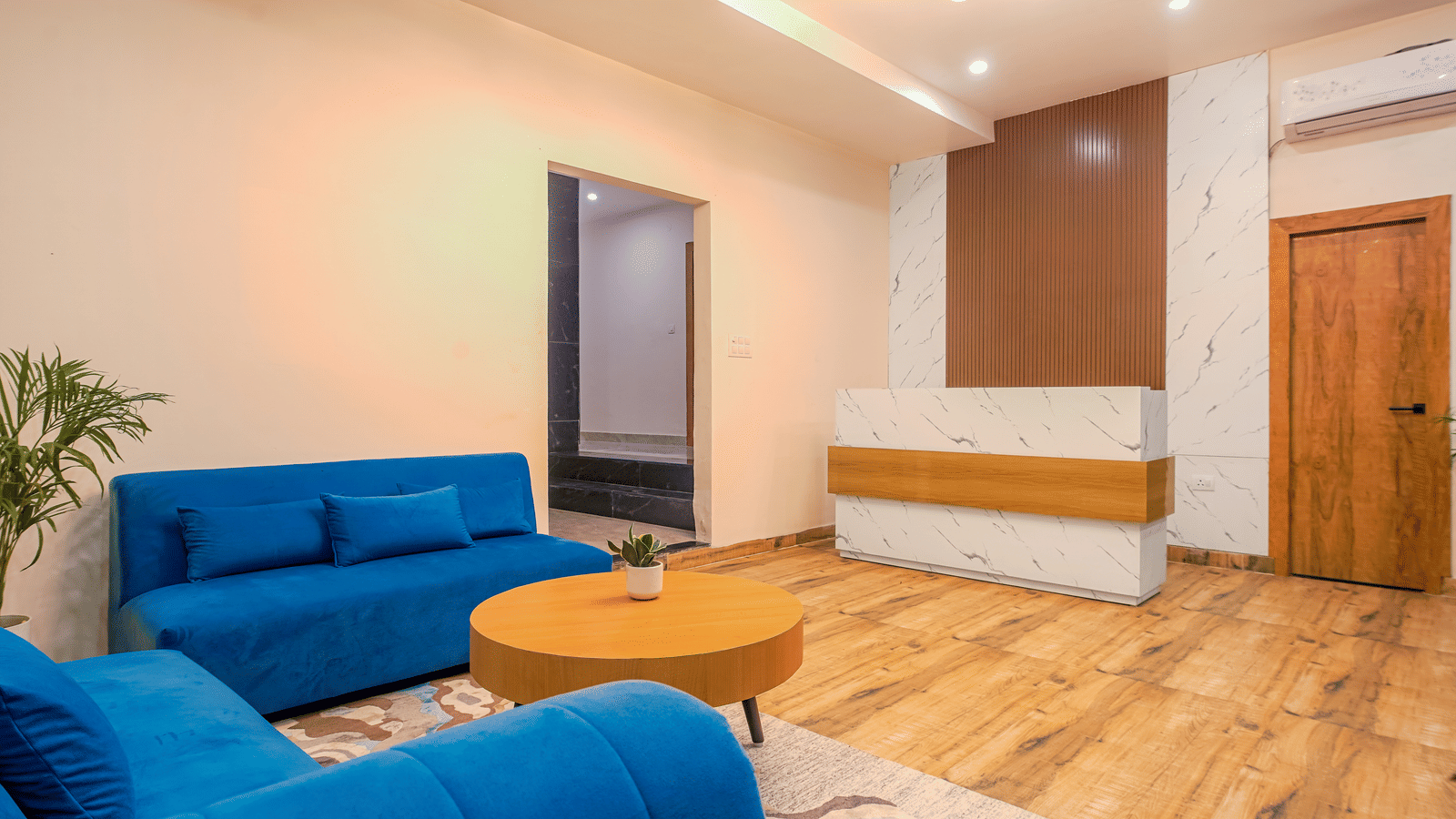 A contemporary hotel lounge featuring a bright blue sofa and a round wooden table in a well-lit room at Perfectstayz Premium Varanasi.
