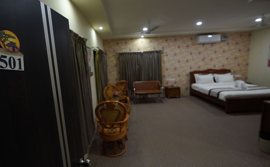 Door opening to Themed Villas of GK Hill View Resort furnished with a double bed, wall-mounted AC, a chair and curtained windows.