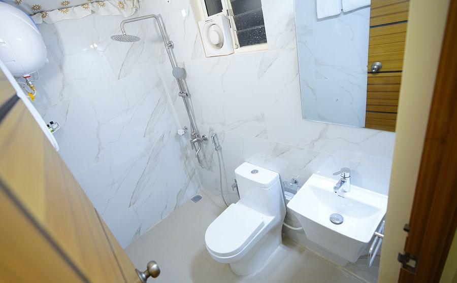 Bathroom of the accommodation in GK Hill View Resort furnished with a sink, western commode, wall-mounter heater, exhaust and shower fittings.