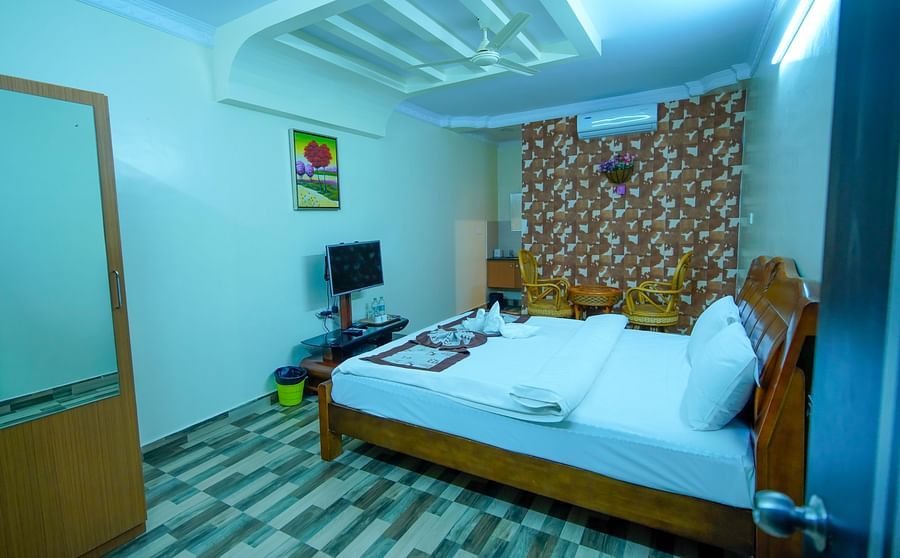 Side view of the Deluxe room furnished with king size bed, sitting area for two, TV, wall-mounted AC and wardrobe.- GK Hill View Resort.