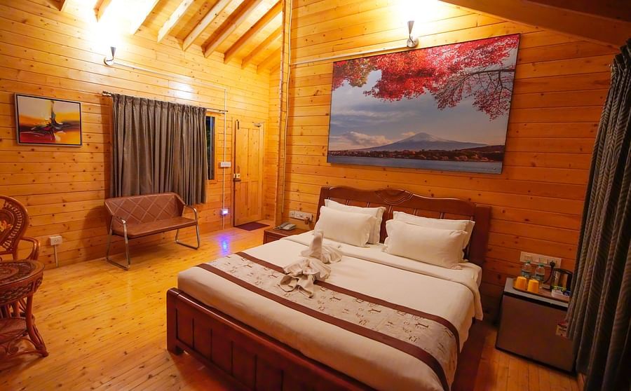 Wooden House of GK Hill View Resort furnished with double bed, sitting chairs, wall-mounted TV, curtained windows and lighting.