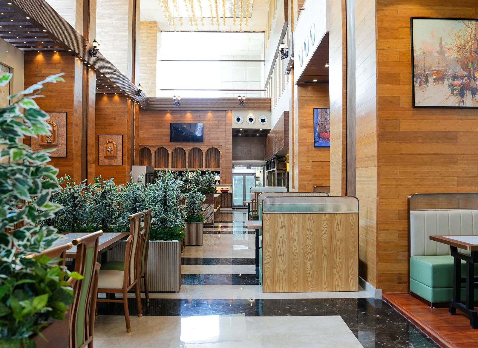 A bright and inviting dining area at The Meriton, adorned with lush green plants, comfortable booth seating in light green, and wooden wall accents.