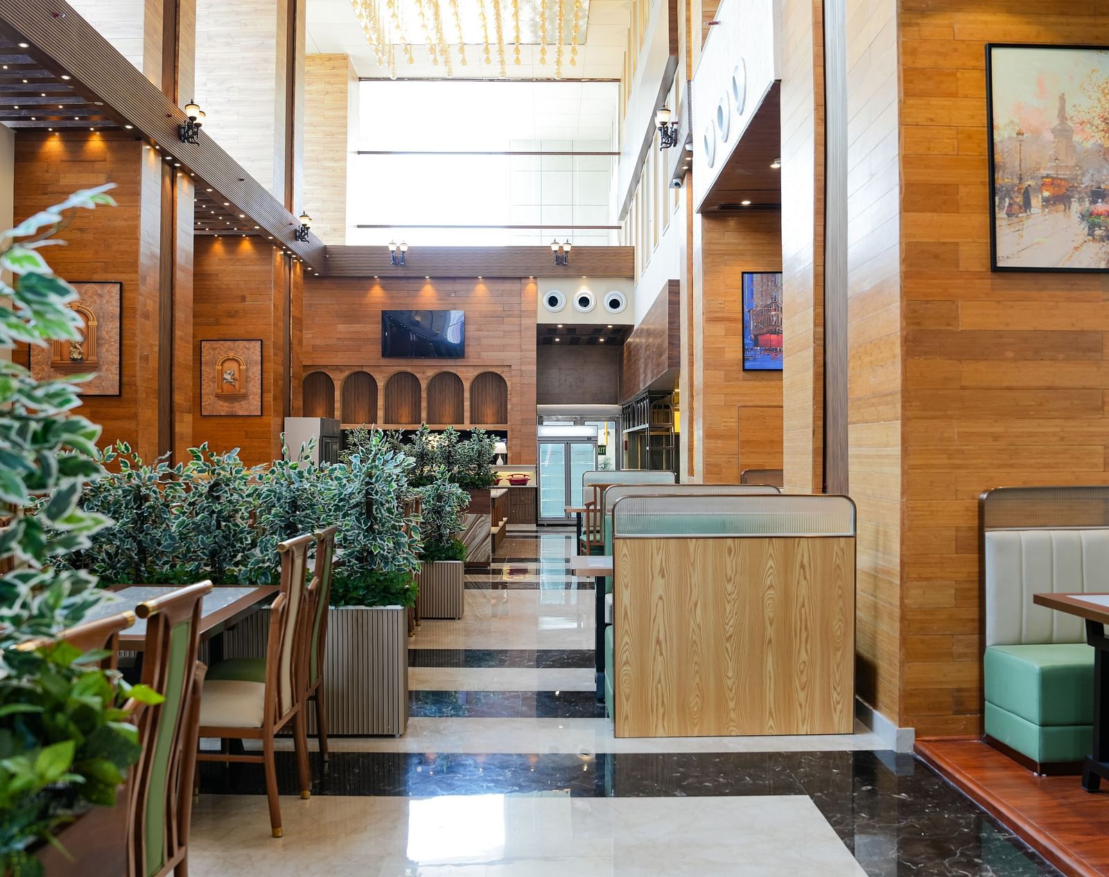 A bright and inviting dining area at The Meriton, adorned with lush green plants, comfortable booth seating in light green, and wooden wall accents.