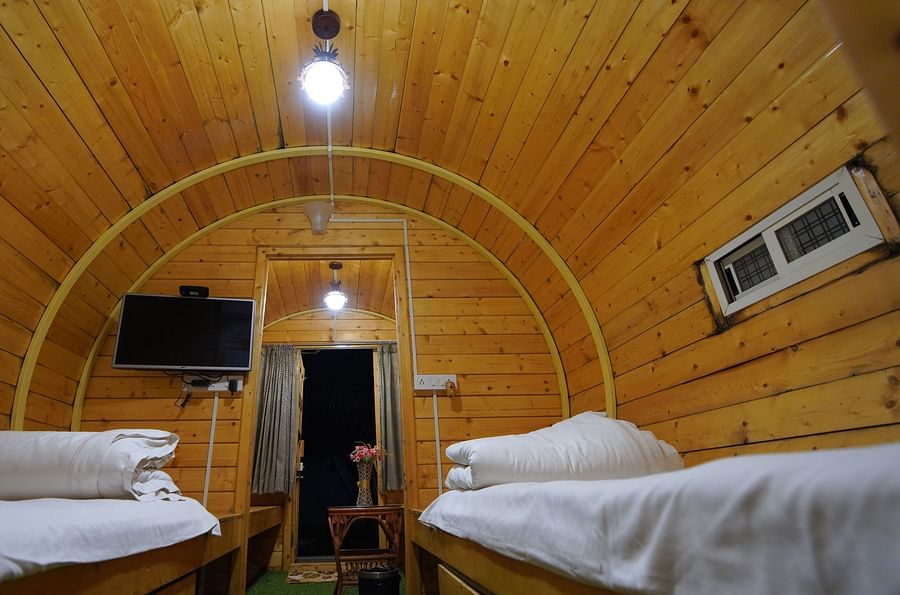Interior of the round-shaped Wooden House at GK Hill View Resort furnished with twin beds, shelves, seating area, wall-mounted TV and overhead lighting.