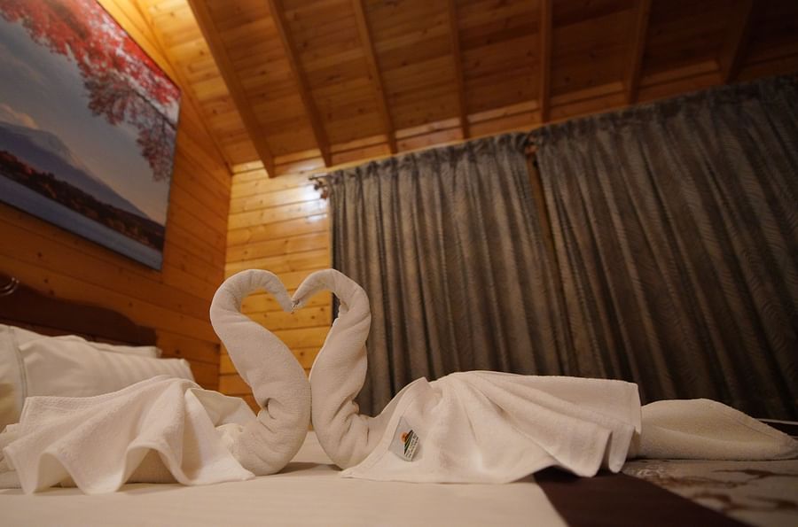 Two swan-shaped turkey towels forming a heart-shape, placed on a bed in the Wooden House of GK Hill View Resort.