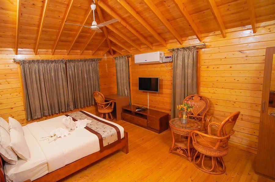 Wooden House of GK Hill View Resort furnished with double bed, sitting chairs, wall-mounted TV, curtained windows and lighting.