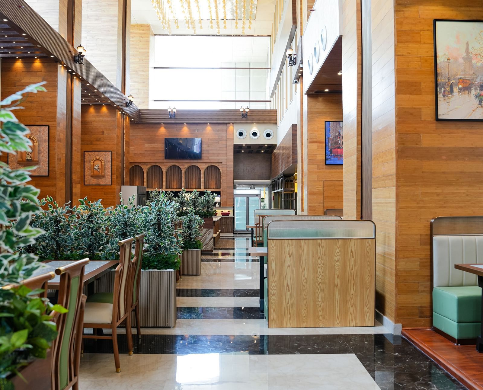A bright and inviting dining area at The Meriton, adorned with lush green plants, comfortable booth seating in light green, and wooden wall accents.