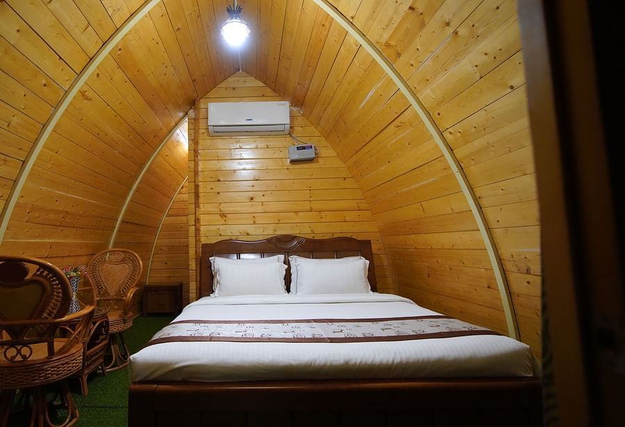 Interior of the A-framed Wooden House at GK Hill View Resort furnished with a king size bed, an intimate sitting area for two, wall-mounted AC and overhead light.