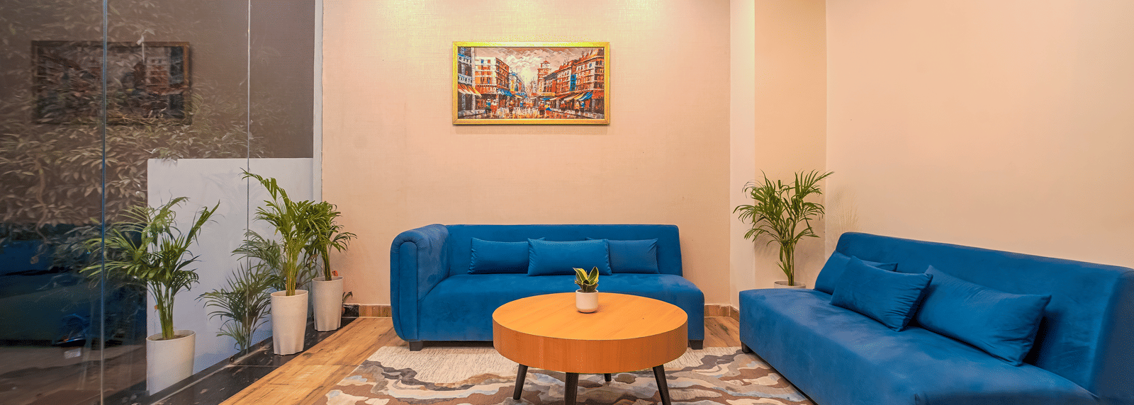 A lounge area at Perfectstayz Premium Varanasi, featuring 2 blue sofa, an artistic wall frame, a round table, and a rug.