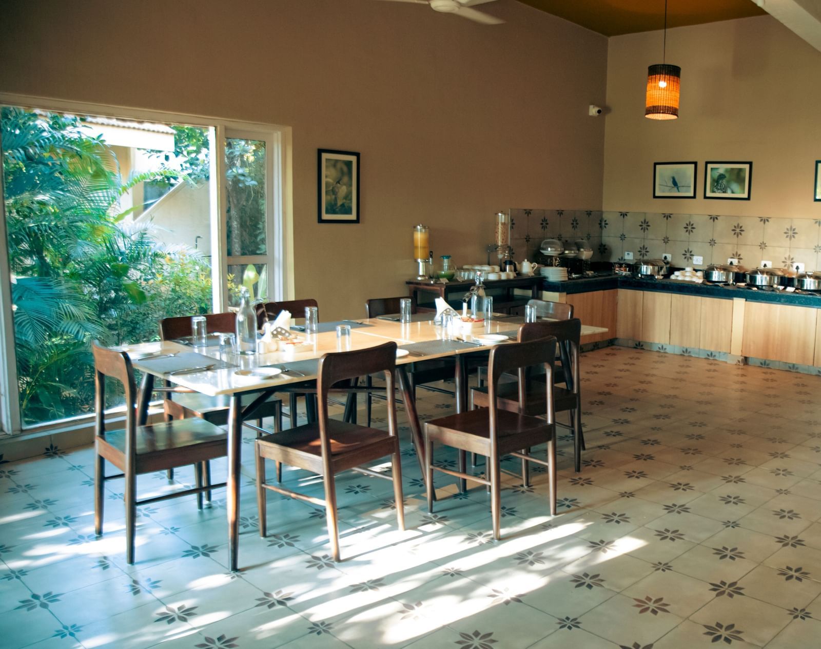Indoor dining area with neatly arranged tables and chairs, wall decor, and natural light entering through large windows at Fireflies Resorts, Kabini.