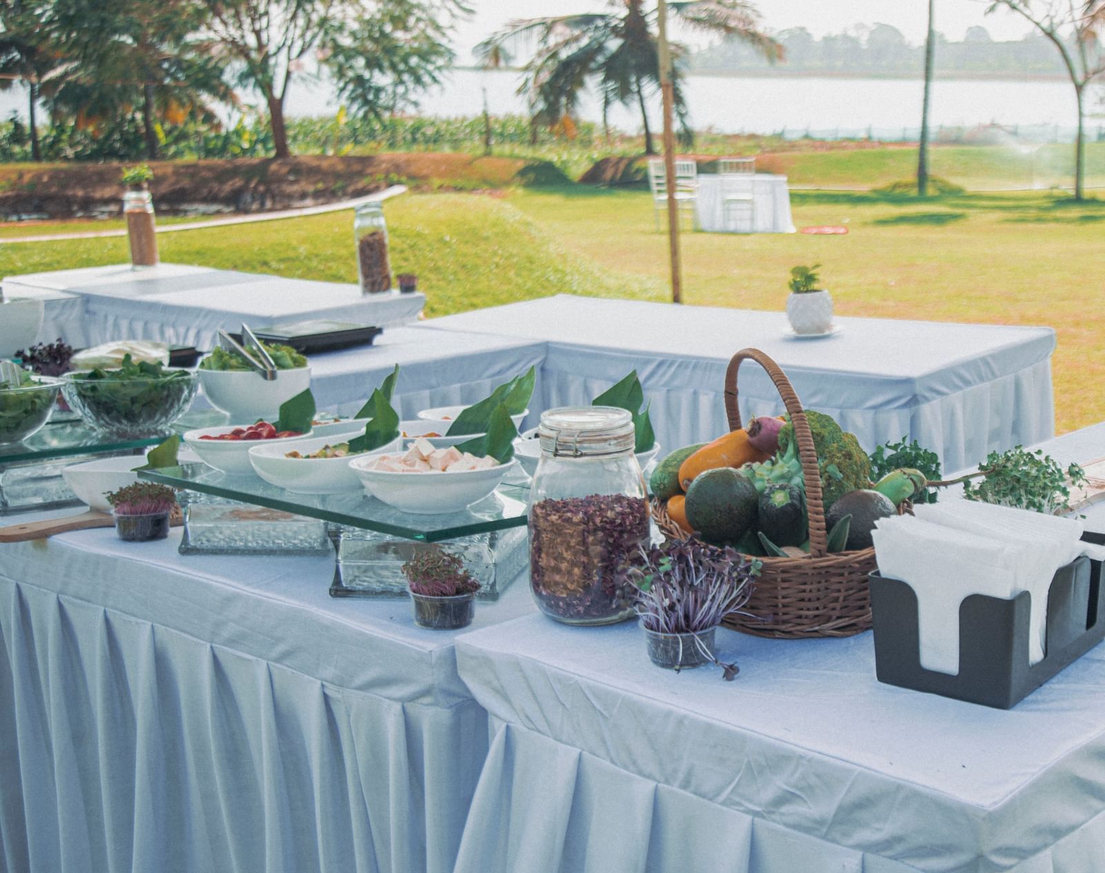 Outdoor buffet arrangement on a lawn with tables covered in white cloth and various condiments displayed at Fireflies Resorts, Kabini.