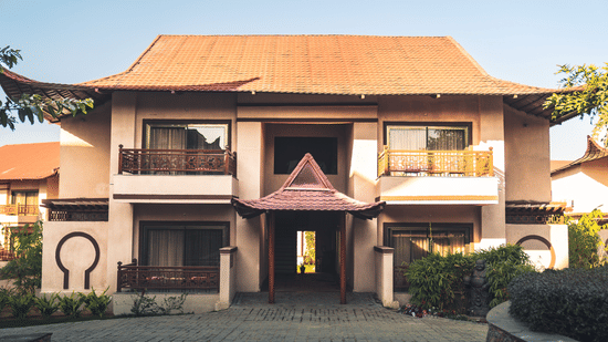 Ananta Spa & Resort, Jaipur exterior featuring a 2-storey villa-style building with balconies, tiled roof, landscaped entrance pathway, and greenery in a peaceful resort setting.