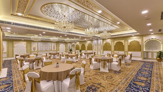 Lavish ballroom with ornate ceiling, multiple chandeliers, and round tables with white and gold accents - Heritage Village Resorts & Spa.