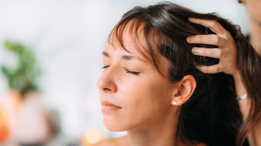 Woman receiving scalp massage with eyes closed in a spa environment.