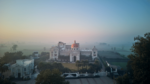 facade of Royal Kingdom Sarovar Portico, Pilibhit with fog-covered fields in the distance