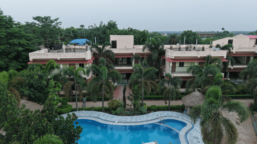 An aerial view of a swimming pool surrounded by green trees and buildings at Shophori Wellness Retreat, Bolpur.