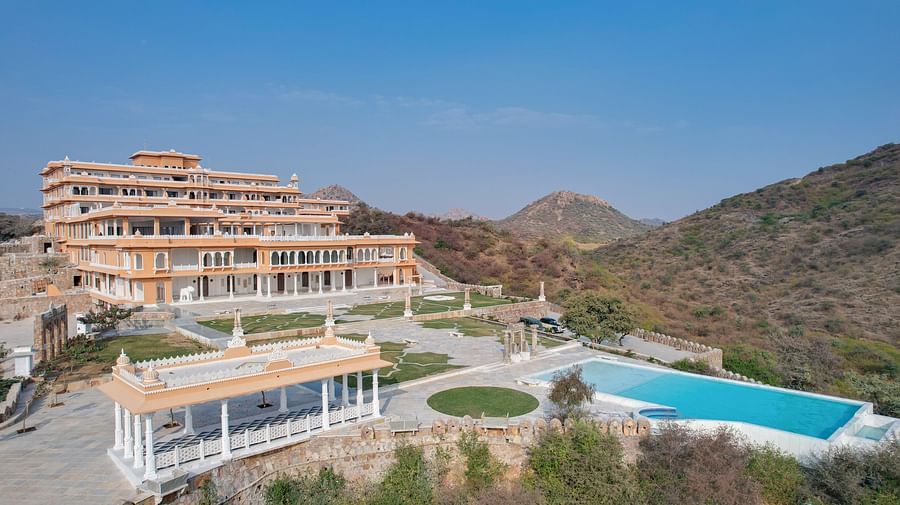 front view of Fateh Vilas with a swimming pool in front of the property surrounded by green mountains