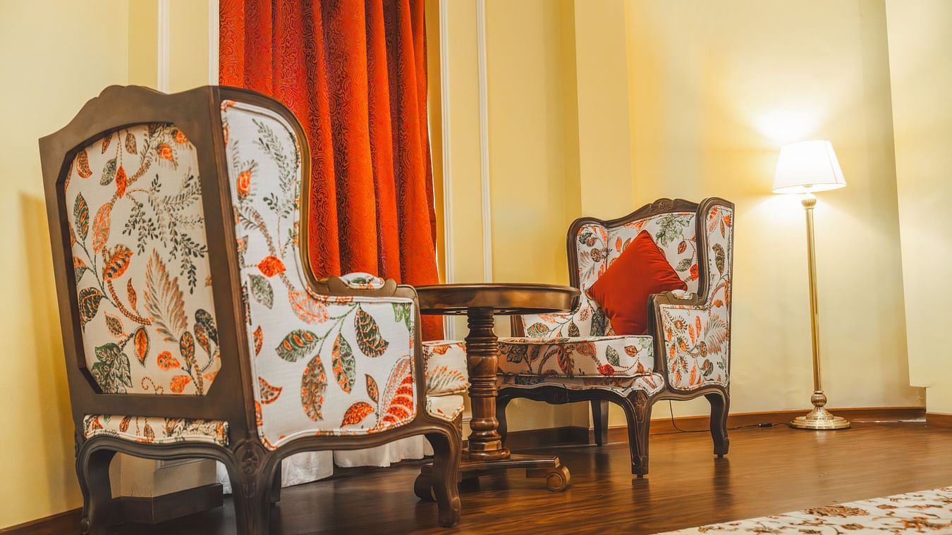Two wooden sofa chairs with comfy cushions facing each other with a wooden teapoy in the middle, at the Super deluxe room at The Garden Ananta Elite.