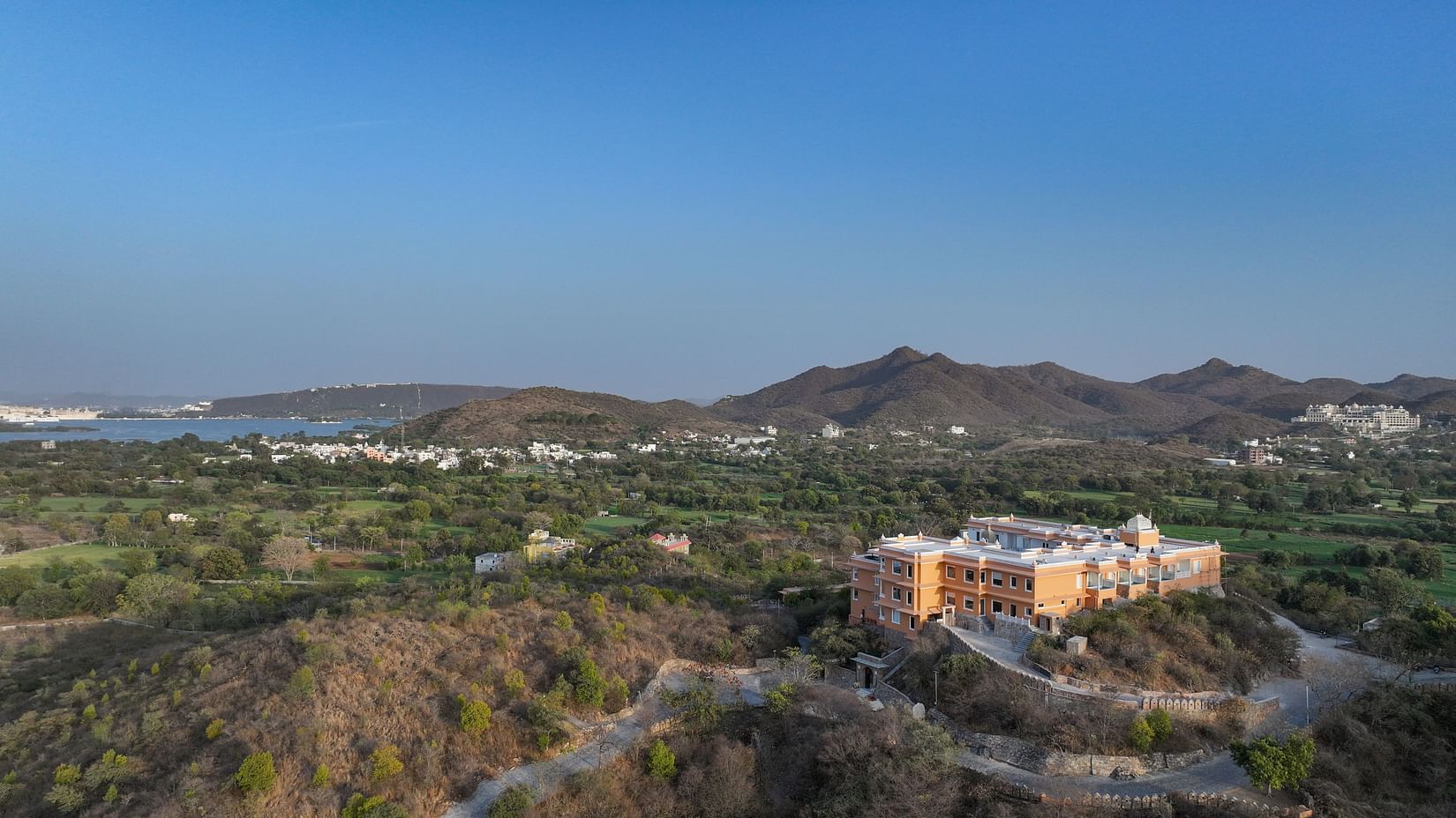 Aerial shot of Khas Mahal by Fateh Collection, Udaipur surrounded by mountains and lush green landscapes.