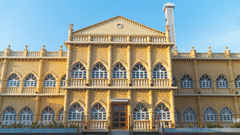 A frontal view of a majestic yellow building with arched windows and a central entryway, set against a clear blue sky - The Garden Ananta Elite, Rajkot