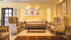An elegant lounge at The Garden Ananta Elite showcases matching ivory sofas and tables, offering a refined space for guests pictured in the golden tint of the lighting.