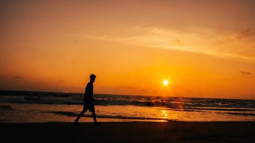 A person walking on the shores of Kovalam Beach with the sun setting in the background.