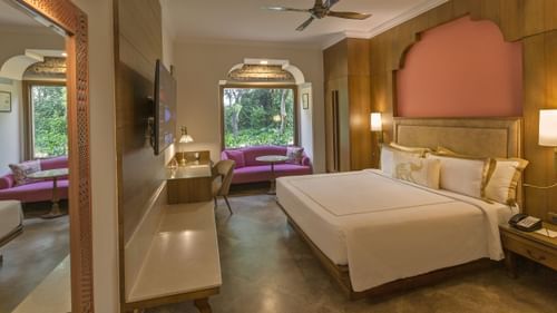 a double bed, side tables with lamps on it and a tv wall mounted opposite it inside premium room - Heritage Village Resorts & Spa, Manesar