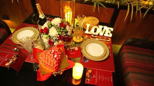 A beautifully arranged table for a romantic dinner, adorned with gifts, fresh flowers, and champagne, with two plates elegantly placed for an intimate meal