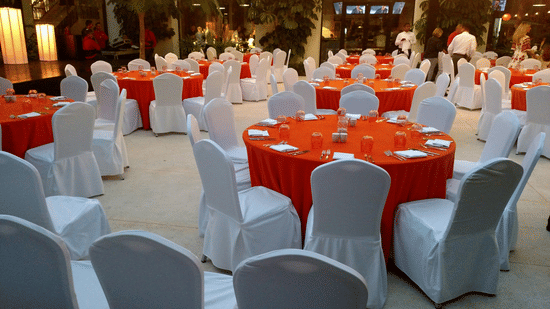 Banquet hall setup with round tables, red covers, and elegant seating arrangement.