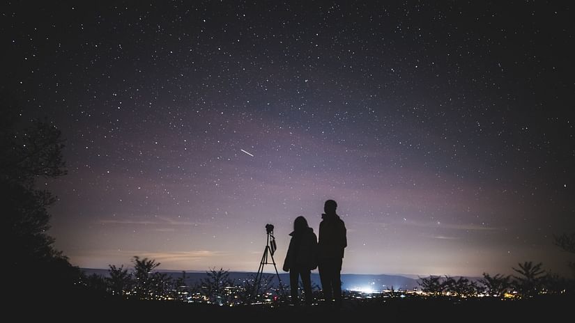 a couple standing on a hill Stargazing with the city skyline in full view