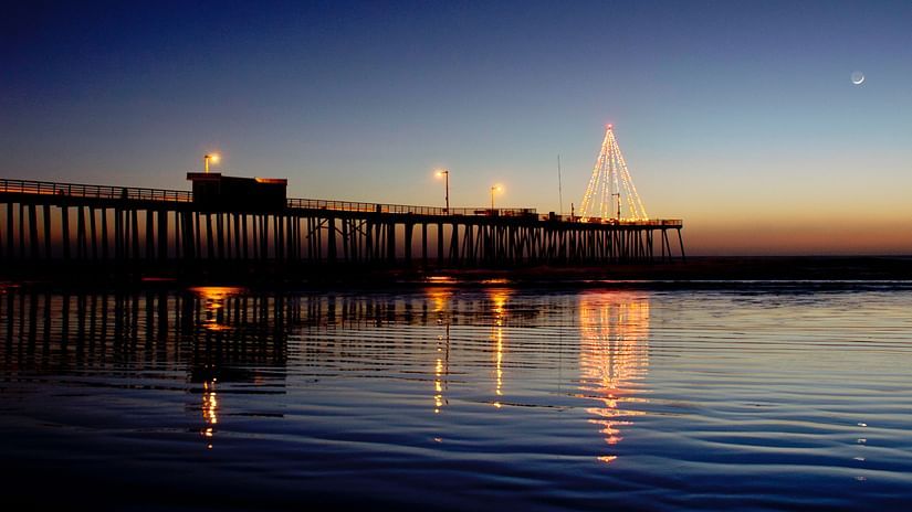 a Christmas tree made out of lights on a boardwalk with the evening sky in the background