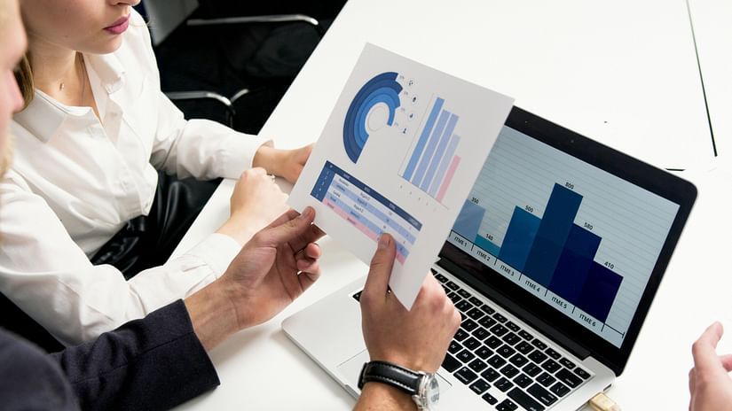Two people discussing a graph held in front of a laptop.