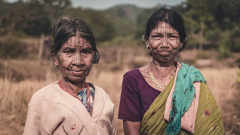 an image of two tribal women posing for a picture amidst the backdrop of a forest