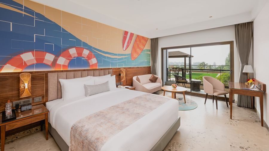 Side view of a bedroom featuring a surf painting above the bed, with a working table and chair at Cloud9 Sarovar Premiere, Palolem Goa.