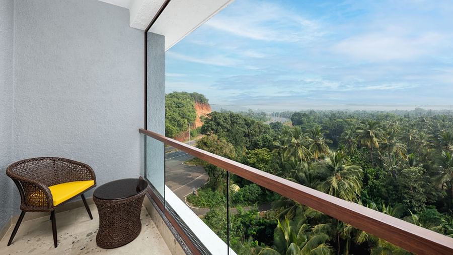 Balcony with a chair and round table offering a view of lush greenery at Cloud9 Sarovar Premiere, Palolem Goa