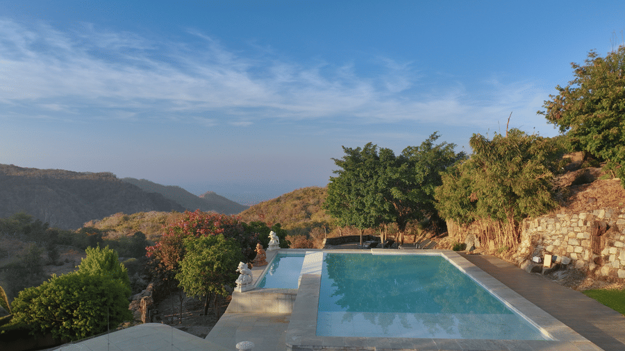 A swimming pool at Fateh Safari Resort, Kumbhalgarh surrounded by plants and trees and offering valley views.