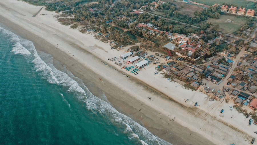 An aerial perspective highlights a sweeping sandy beach meeting turquoise ocean waves and green land.