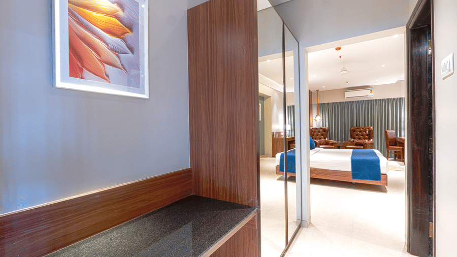 A room entrance showing a built-in wooden desk, a mirror, and a bed featuring blue accents at Magnus Kapitol, Sakore Nagar, Viman Nagar.
