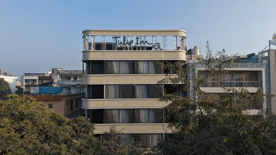 A daytime exterior view of the Tulip Inn Gurugram building showing its multi-story facade and rooftop signage above surrounding trees.