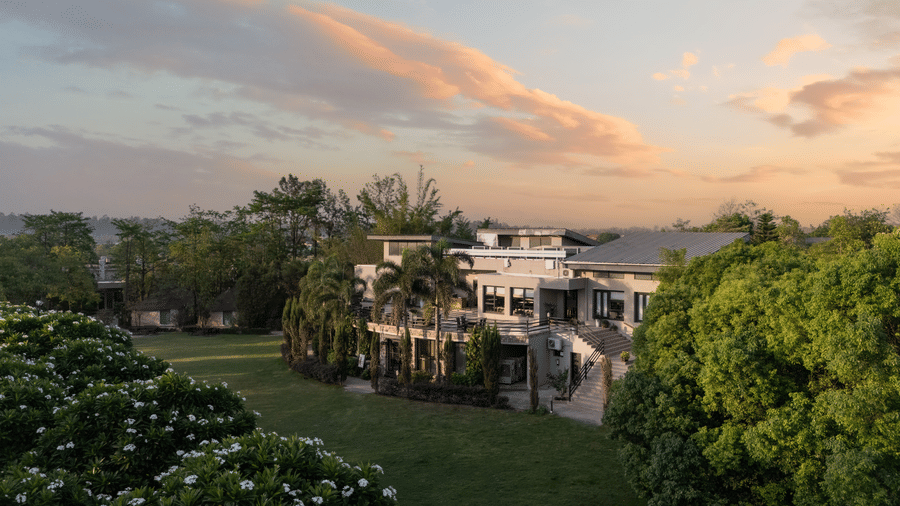Resort building in the distance, surrounded by green lawns and trees at sunset at The Golden Tusk, Jim Corbett