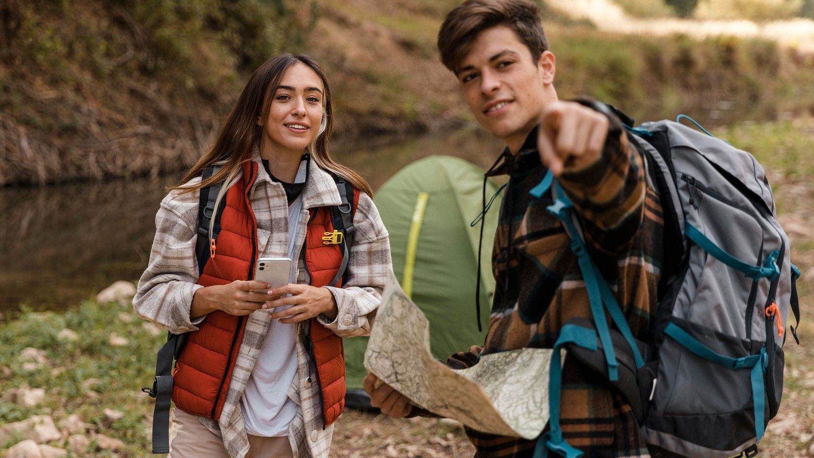 Two people standing in a forest, facing the camera, holding a map and pointing in the direction.