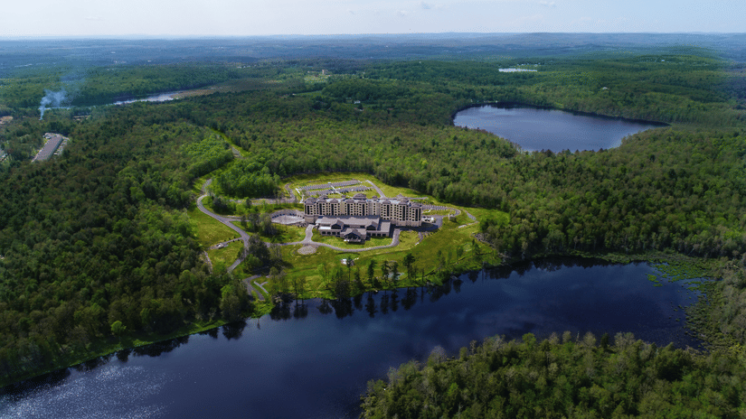 Exterior view of YO1, Catskills, New York, showcasing its modern facade surrounded by lush greenery and a lake.