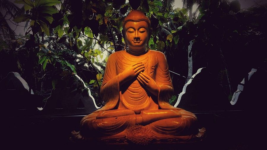 A statue of Buddha with rocks and greenery behind