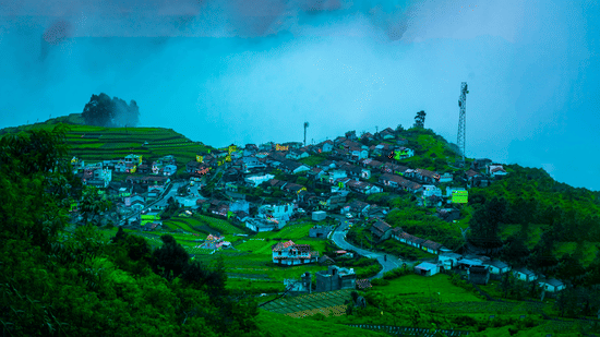 Hilltop settlement covered in mist, featuring clustered houses and a communication tower overlooking the valley in Kodaikanal, Tamil Nadu.