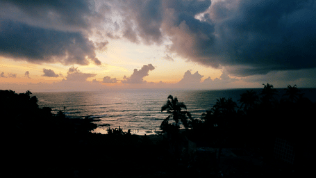 A view from the land of a beach in Goa with many people on the shores and dark clouds above. These beaches can be one of the best places to visit in South Goa during monsoons.