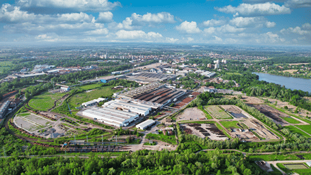 Aerial view of a sprawling IT park, Nagpur, surrounded by green fields and trees under a cloudy blue sky.