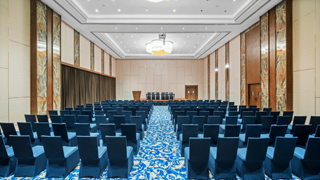 Champavati party hall in Vijayawada featuring blue theatre-style seating, elegant chandeliers, a central aisle, and spacious interiors | Grand Vijayawada by GRT Hotels