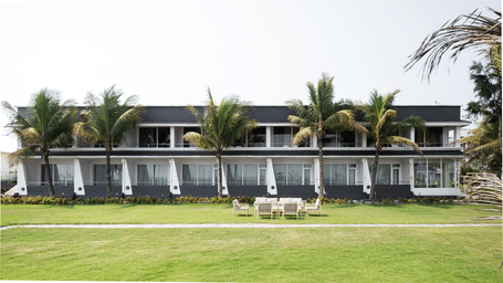 A wide shot of Hotel Sonar Bangla, showing a long lawn with seating and palm trees.
