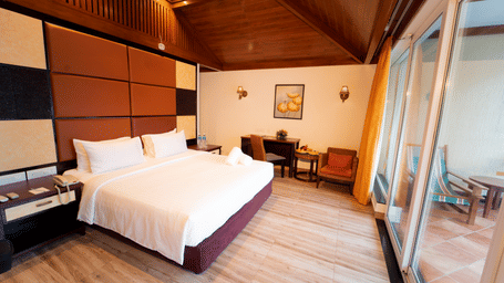 Bedroom in Santtorini Villa at Ocean Spray, one of the best places to stay in Pondicherry, featuring a bed, pillows, wall panels, a side table, chairs, a desk, wall lights, a framed picture, a window, curtains, and a balcony.